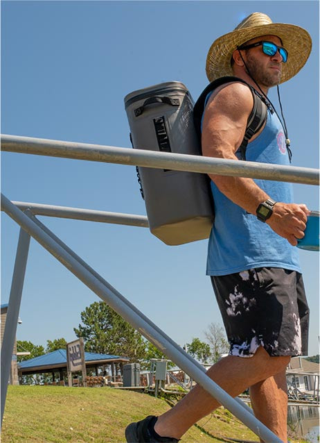 A man wearing a 25L light grey backpack soft cooler and carrying a 14oz coffee mug while walking down a dock ramp.