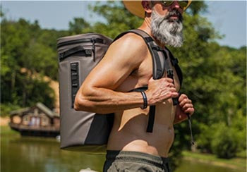 A man carrying a 25L Backpack Soft Cooler next to a lake.